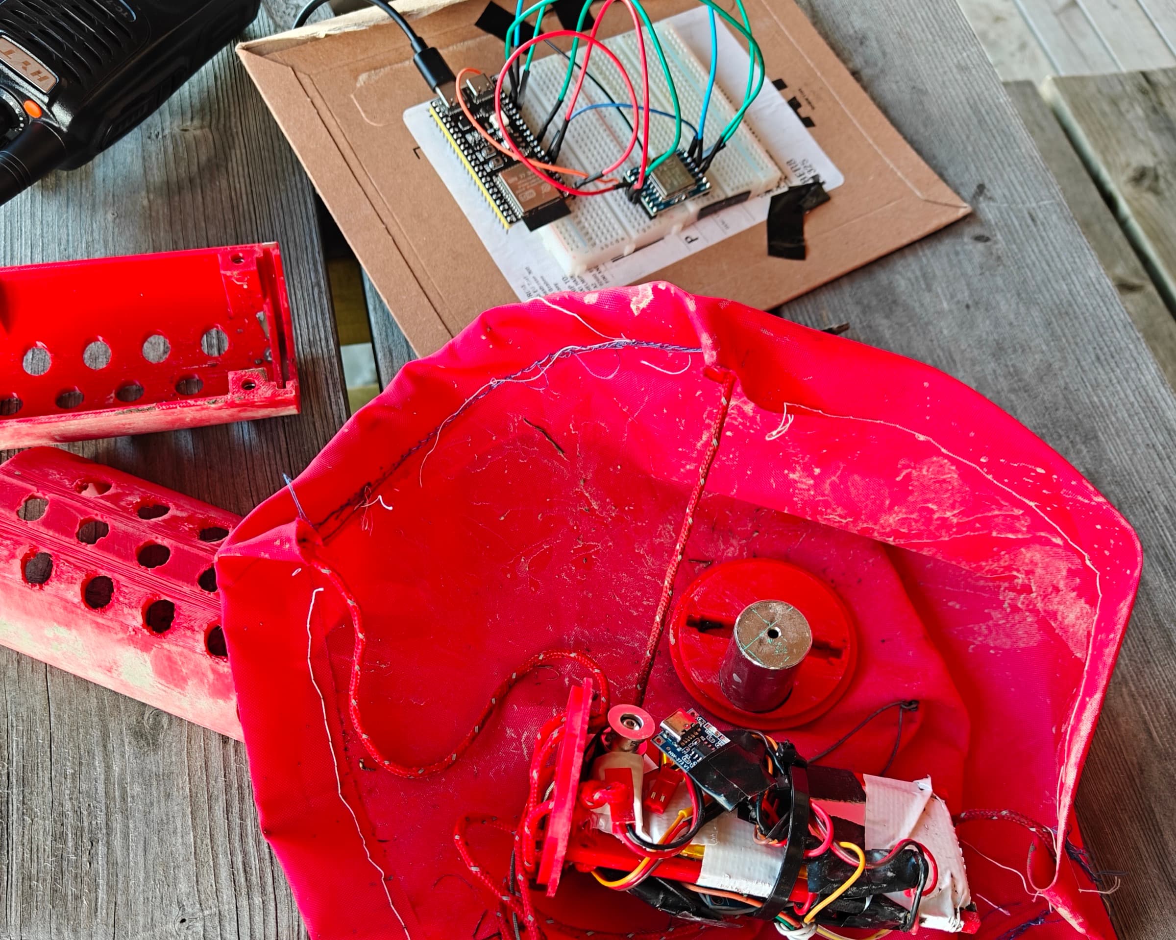 Otis-1 back on the ground: the can on its parachute, still muddy, with the ESP32 ground-station breadboard and the radio behind it.